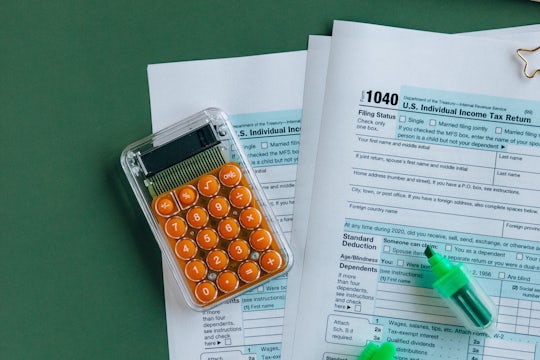 Tax Form 1040 sits on a table with a calculator and a green highlighter