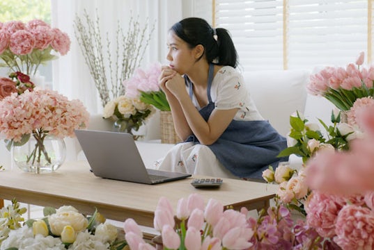 Business owner sits in her flower shop at her computer looking worried