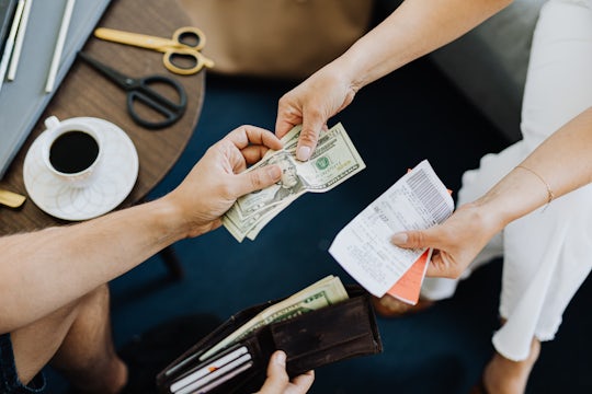 Two people sit a desk with coffee and count money over a set of receipts