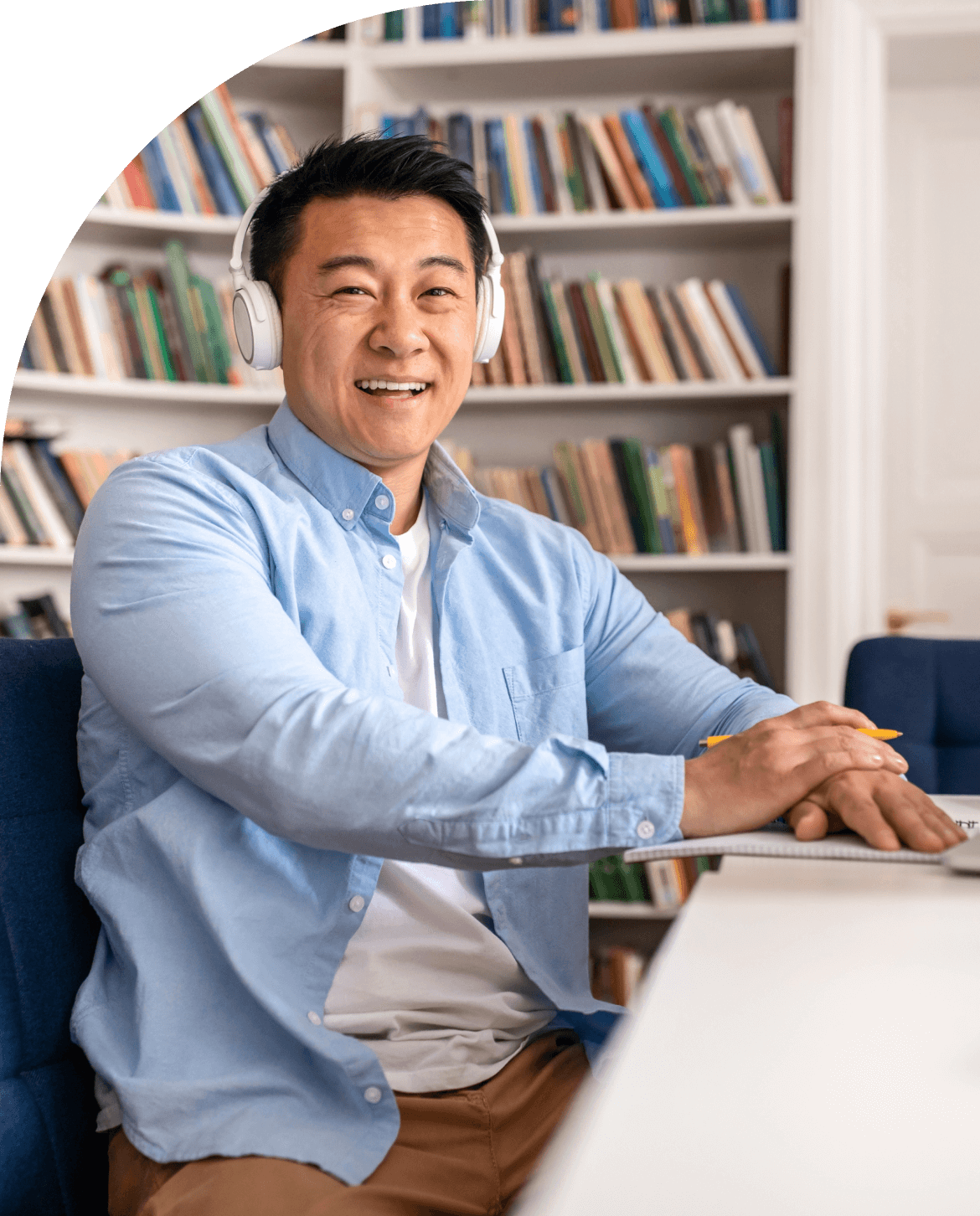 Photo of a man wearing white headphones in a blue unbuttoned shirt who is taking notes