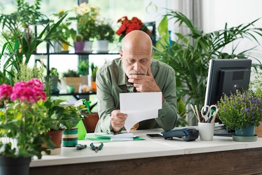 flower shop owner looks worried while studying a letter