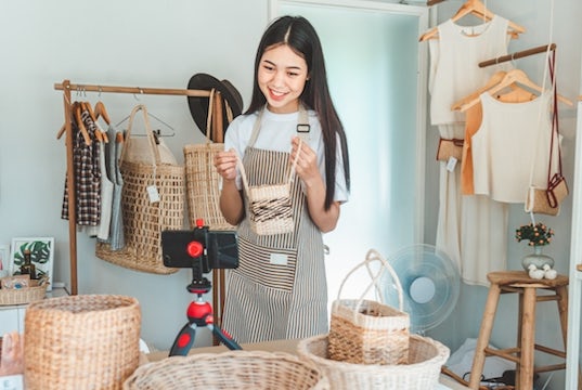 Digital creator holds up a handbag to her camera to create content for her social media channel