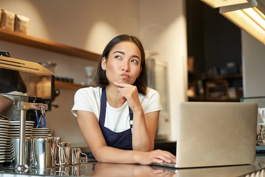 Barista a coffee shop works at her computer while pondering some questions