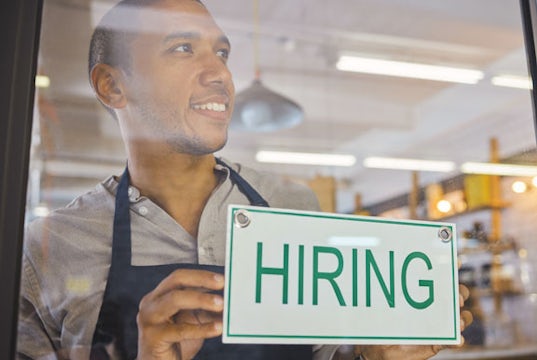 African-American man hangs a hiring sign in the window of his small business