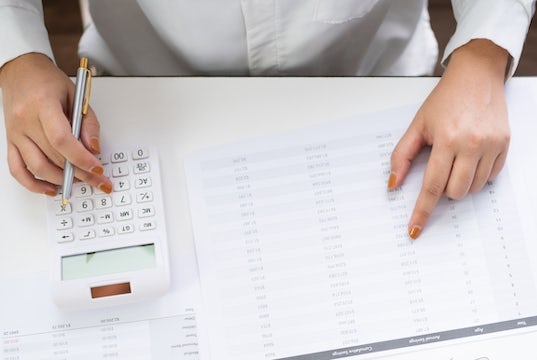 Overhead view of businesswoman's hands working on a ledger with a calculator