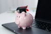 Piggy bank with a graduation cap sits on top of a laptop