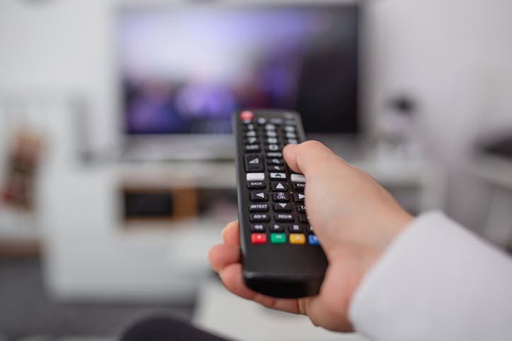 Pessoa com controle remoto na mão apontando para a TV