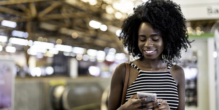 Mulher sorri enquanto usa o celular na rua