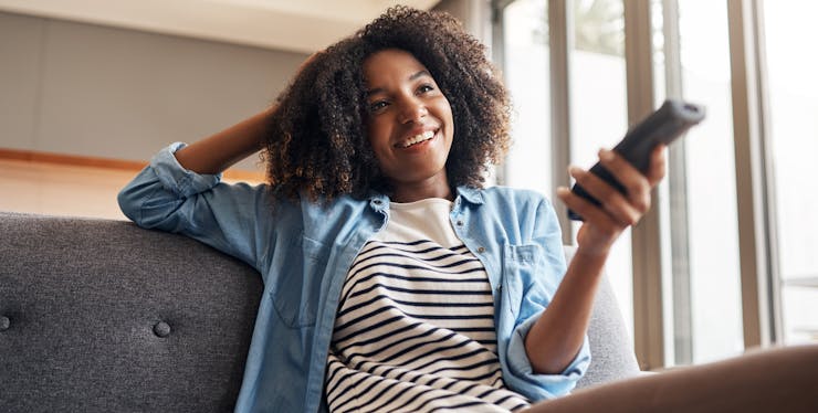 mulher assistindo TV por assinatura enquanto segura controle remoto