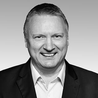 Ein lächelnder Mann mit weißem Hemd und schwarzem Sakko.