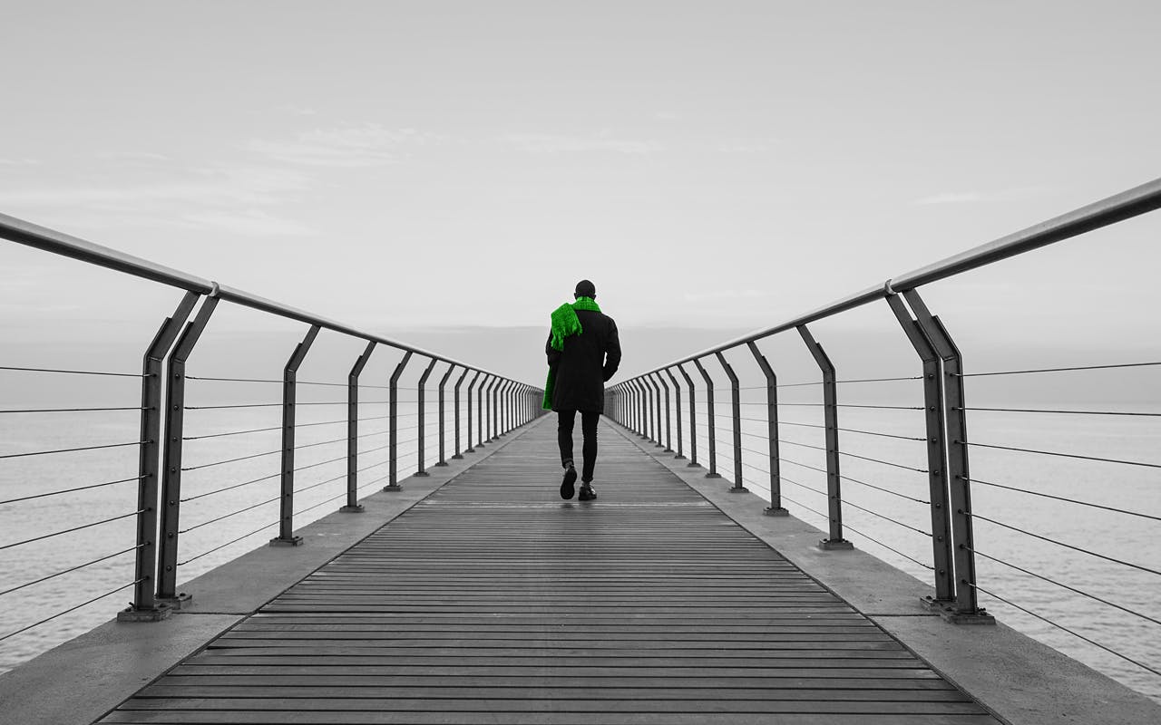 Ein Mann in schwarzem Anzug und grünen Schal, der einen Steg entlang läuft.