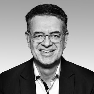 Ein lächelnder Mann mit Brille und schwarzem Sakko.