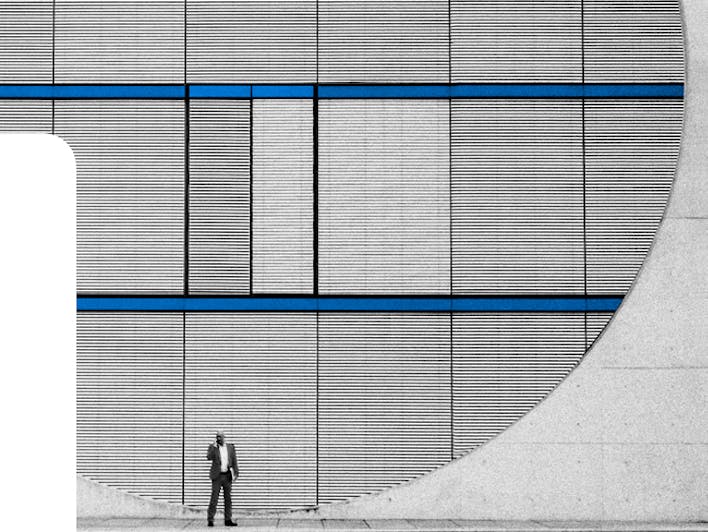 A person in a suit walking along a blue-gray wall of a house.