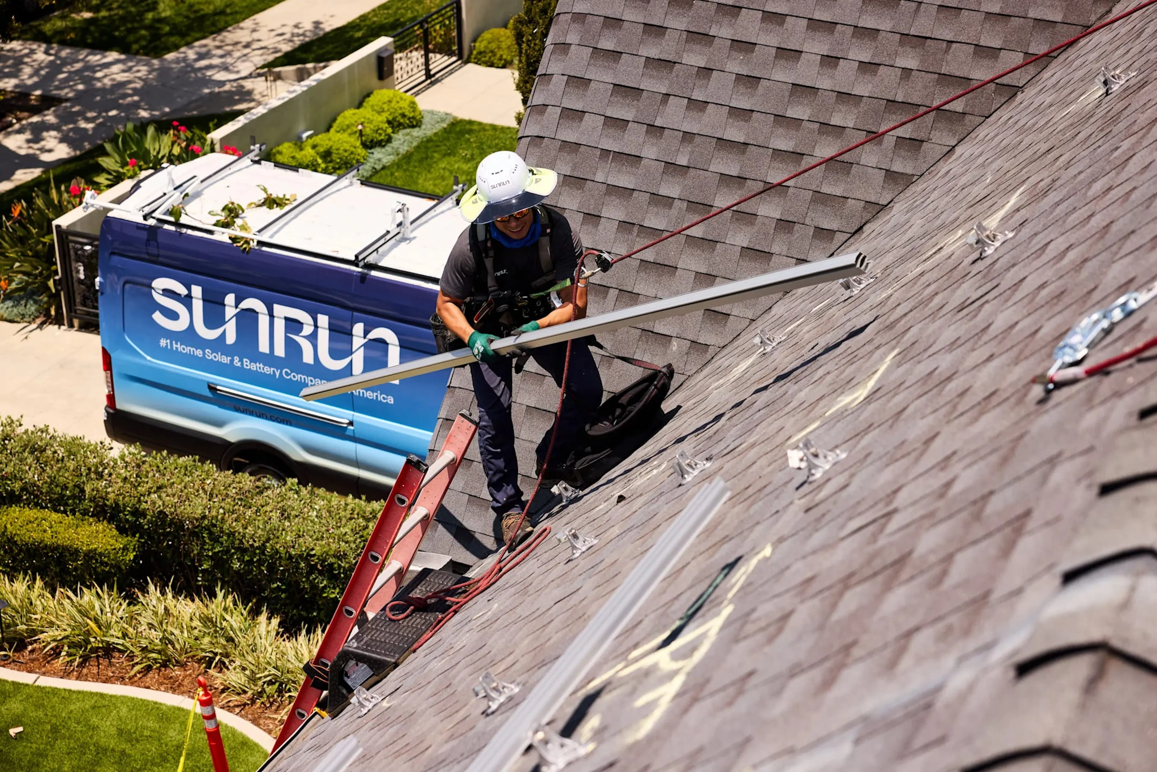 A Sunrun truck sits in a driveway, with crew members on the home's roof installing solar panels.