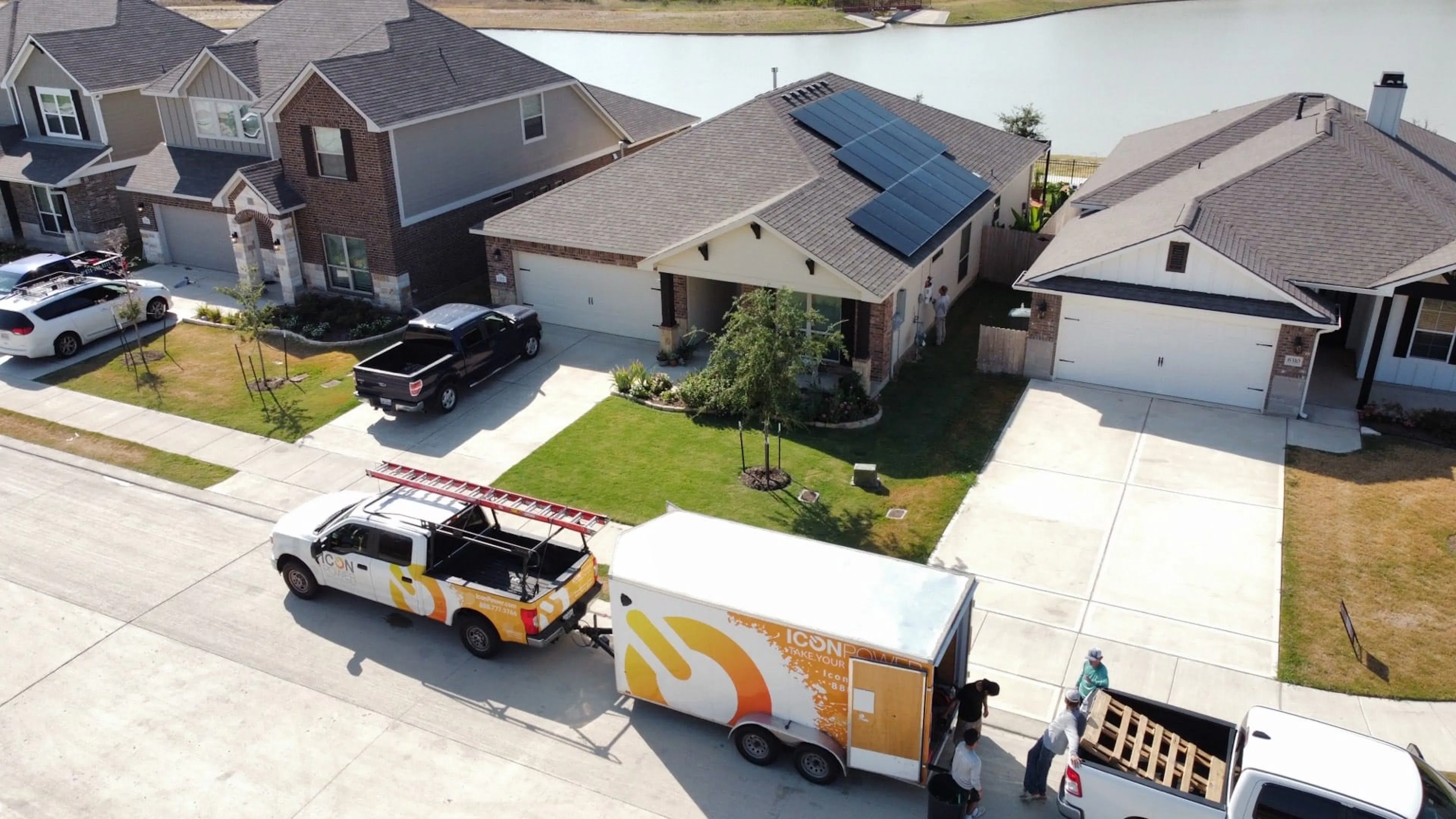 Trucks branded with Icon Power sit on the side of a residential street in front of a home with solar panels on the roof.