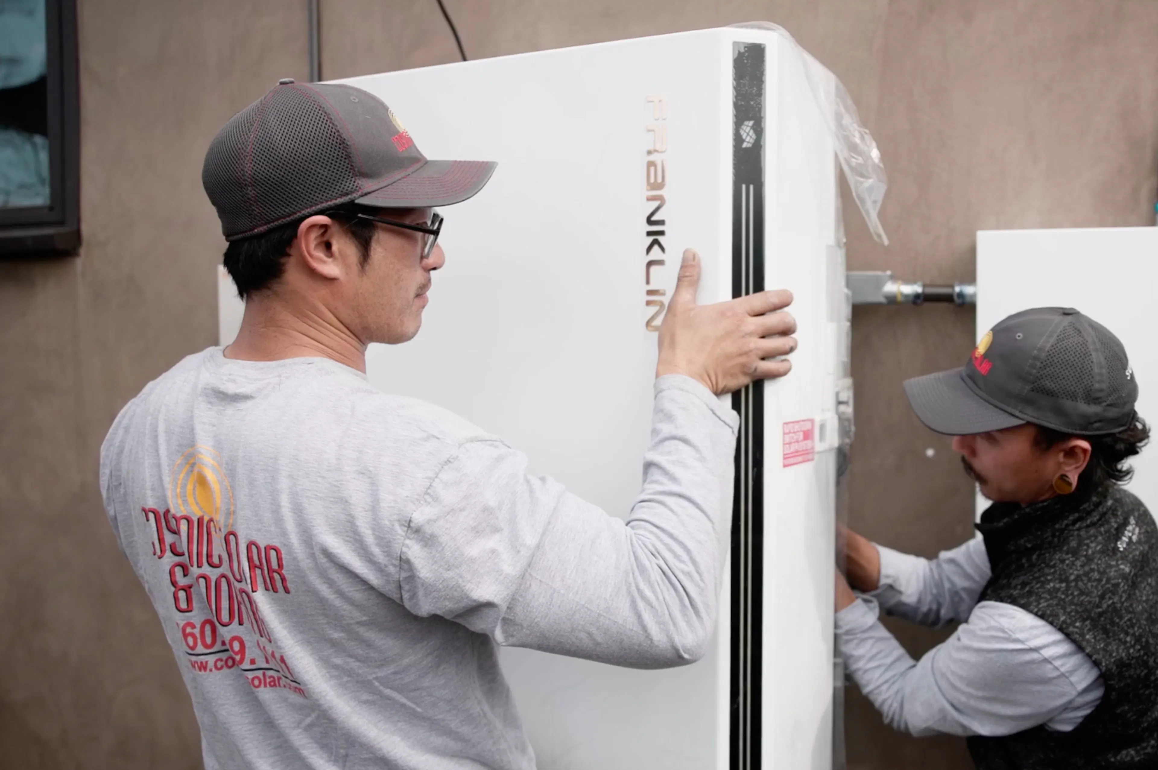 Crew members from Cosmic Solar mount a FranklinWH battery on the wall of a home.