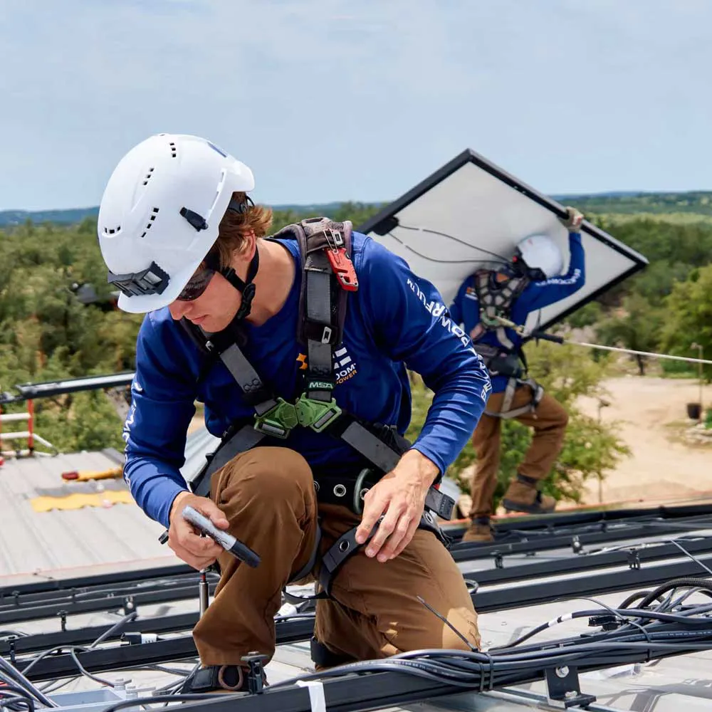 A solar installation crew member from Freedom Power on a home's roof, mounting a solar panel.