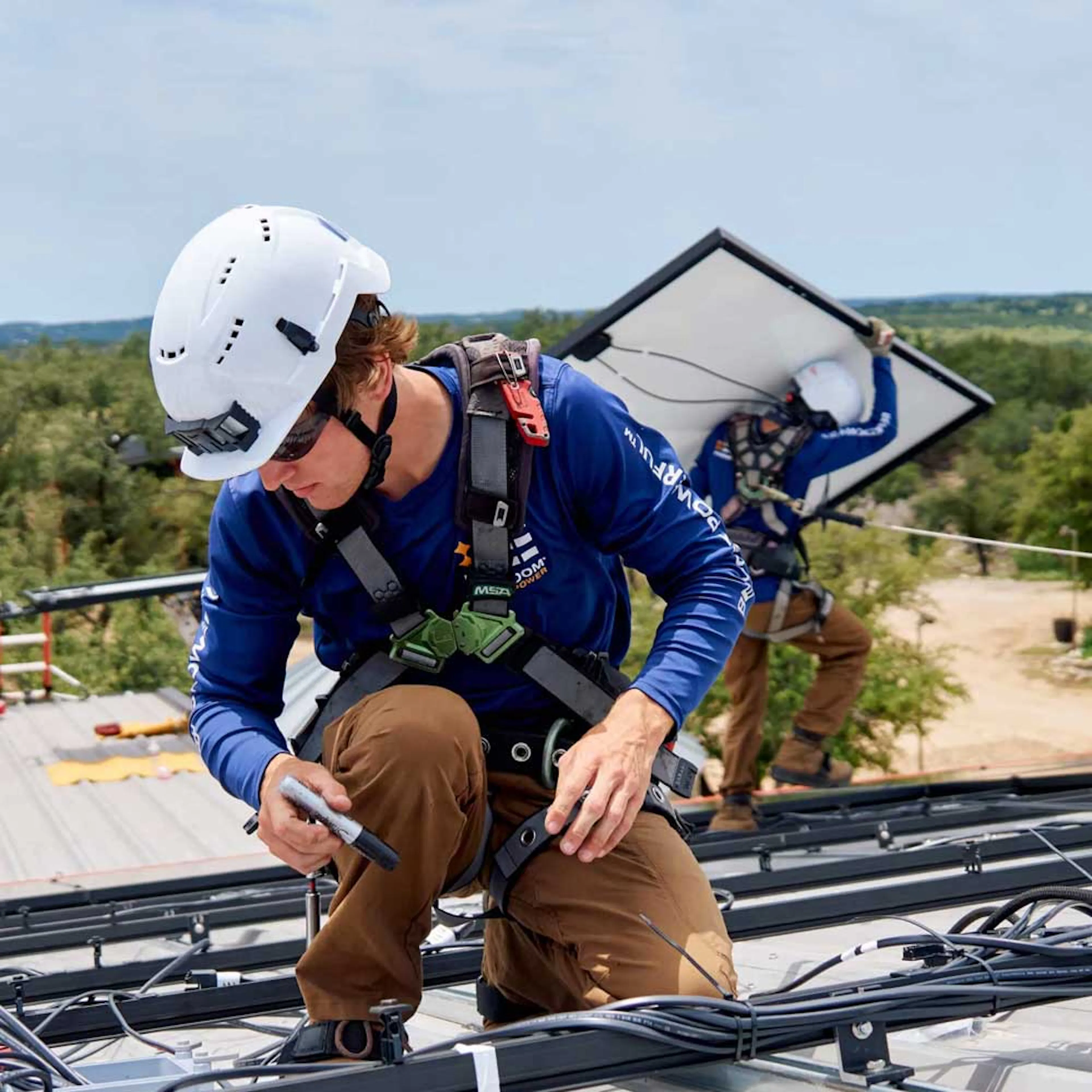 A solar installation crew member from Freedom Power on a home's roof, mounting a solar panel.