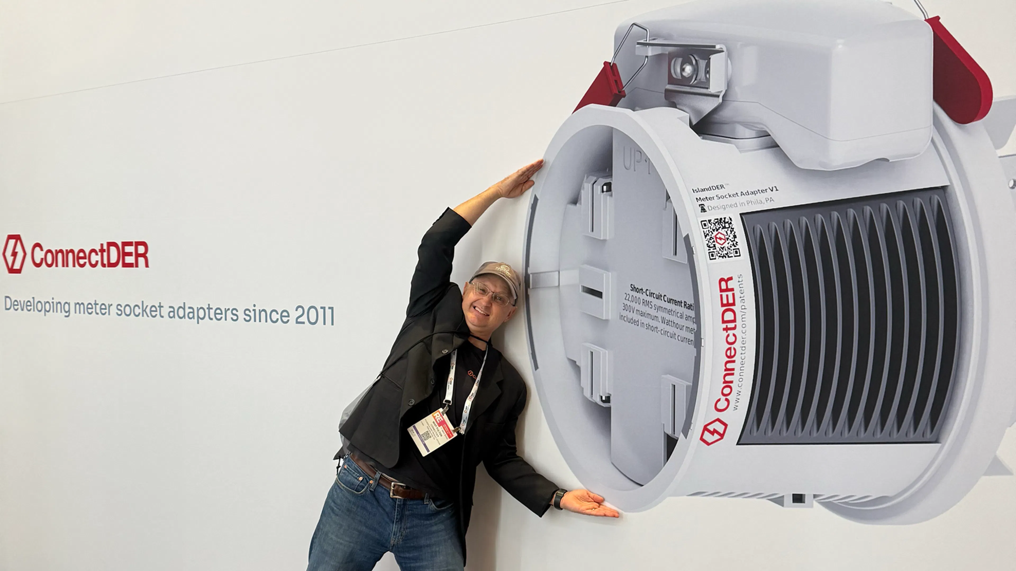 ConnectDER's founder Whit Fulton stands next to a graphic of a massive meter socket adapter.