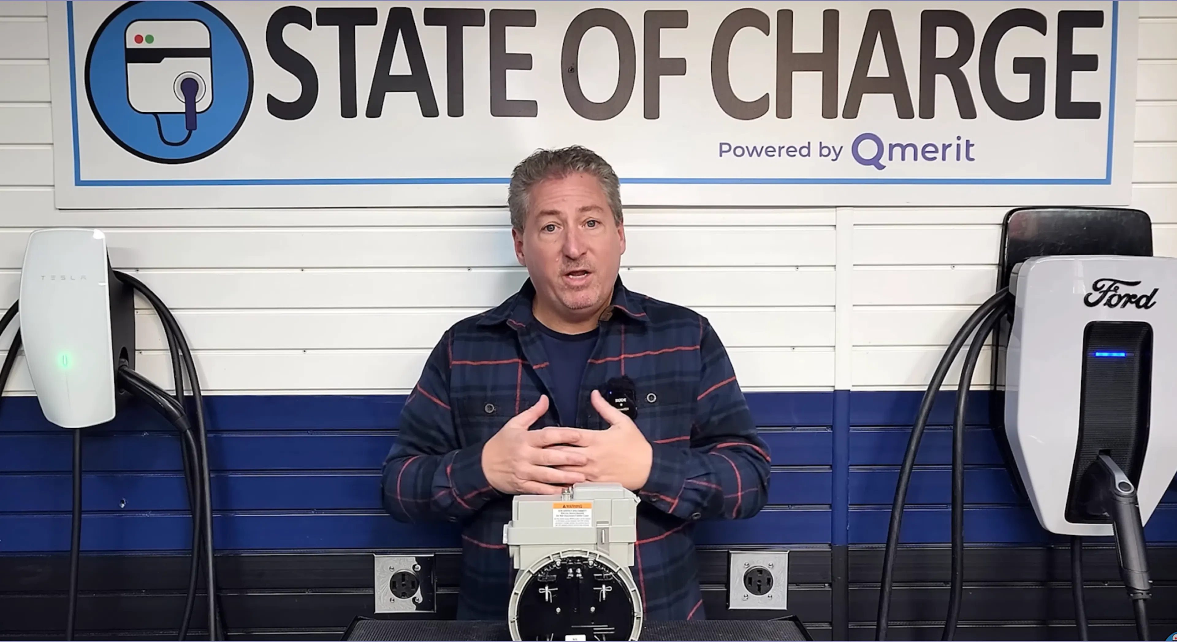 The host of the YouTube channel State of Charge stands in his workshop with a ConnectDER EV Meter Socket Adapter on the table in front of him.