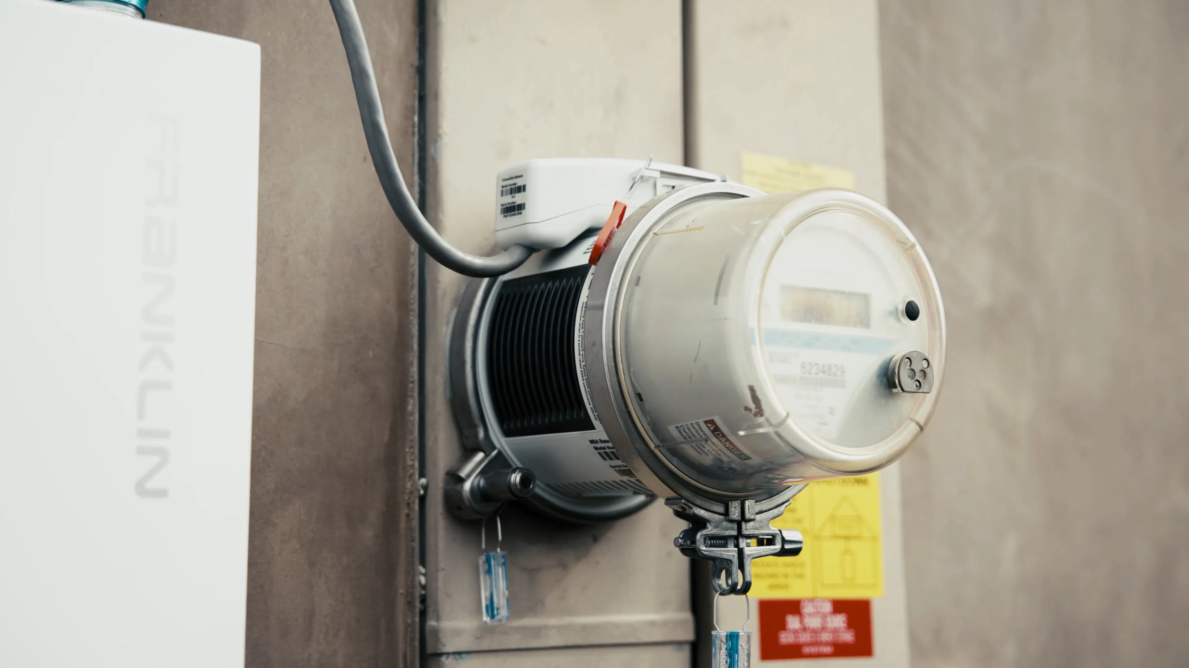 A close-up photo of the ConnectDER IslandDER™ MSA in a utility meter socket, with rain drops on it, next to a FranklinWH battery storage system on the wall of a home.