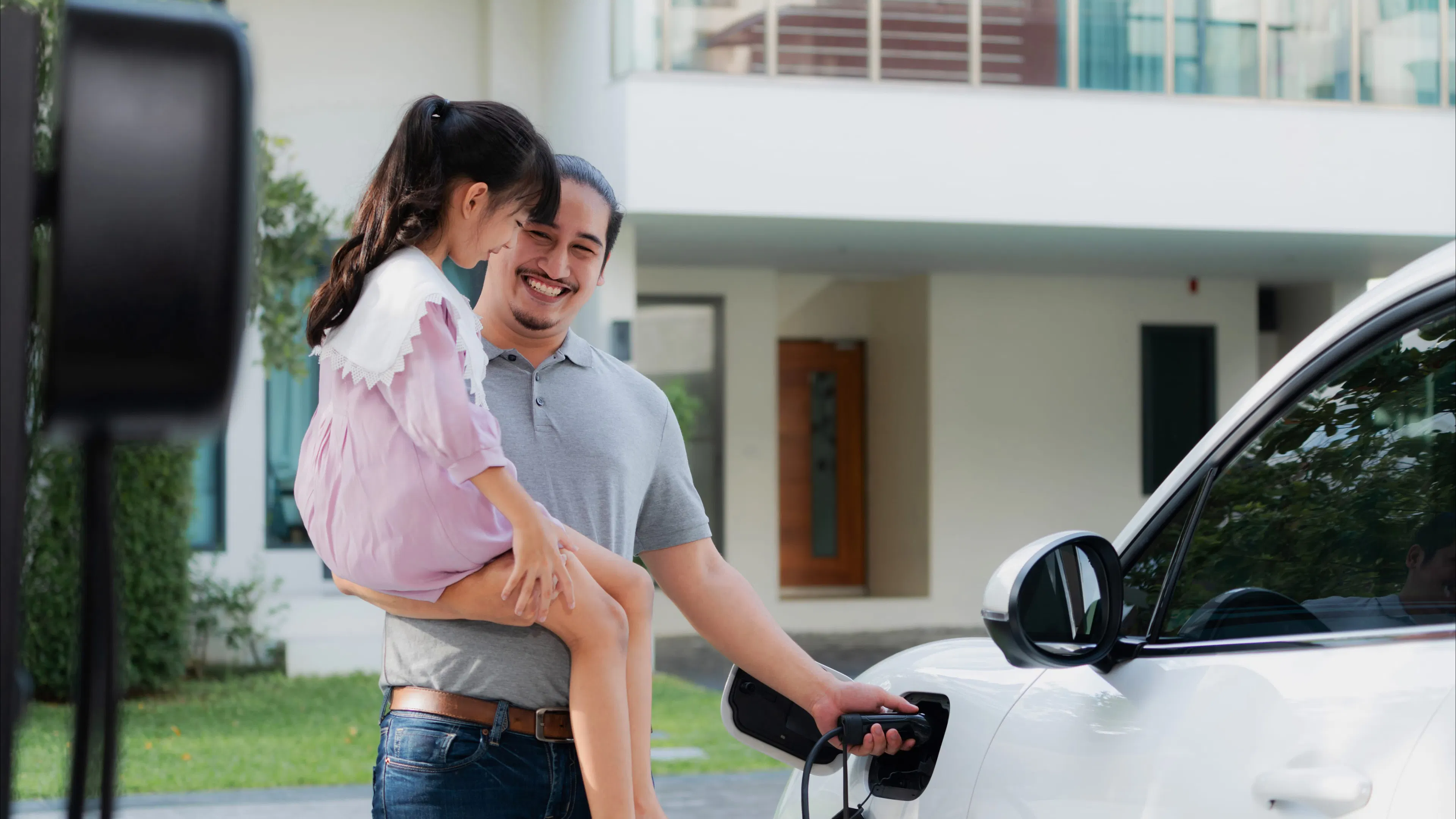 A homeowner charging his electric vehicle in his driveway, holding his daughter.