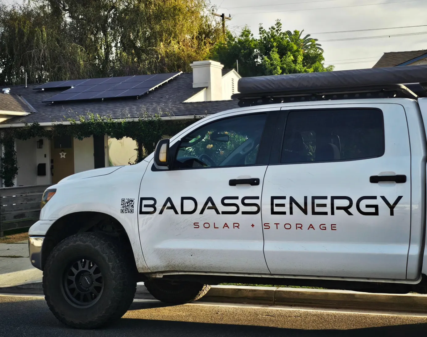 A truck with Badass Energy branding sits in a driveway of a home with solar panels on the roof.