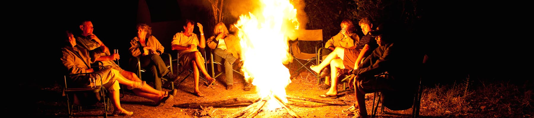 A group of ACE volunteers and staff gathered around a camp fire at night time in the African bush