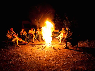 A group of ACE volunteers and staff gathered around a camp fire at night time in the African bush