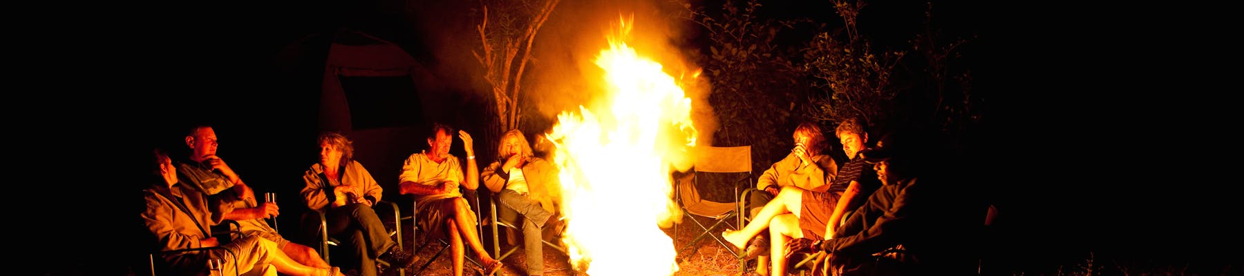 A group of ACE volunteers and staff gathered around a camp fire at night time in the African bush