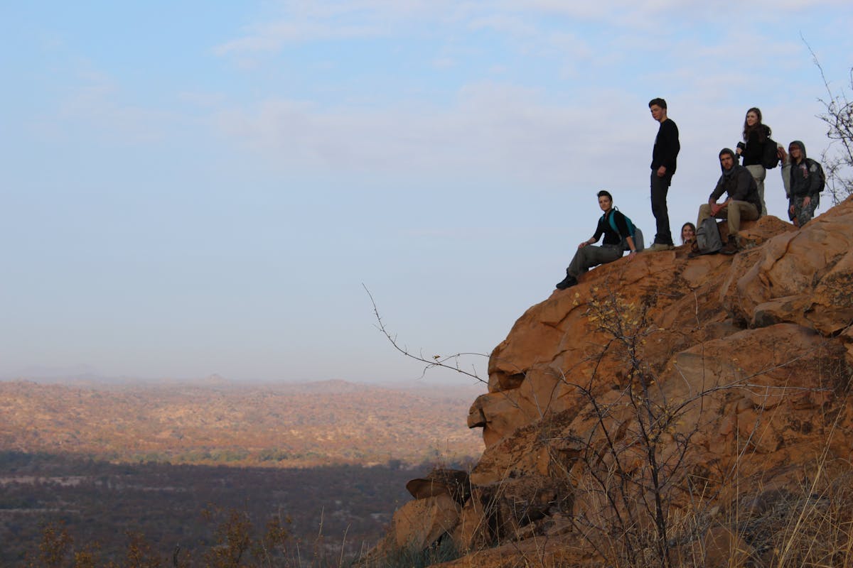 A group of students are perched on the edge of a cliff, observing the view and relaxing