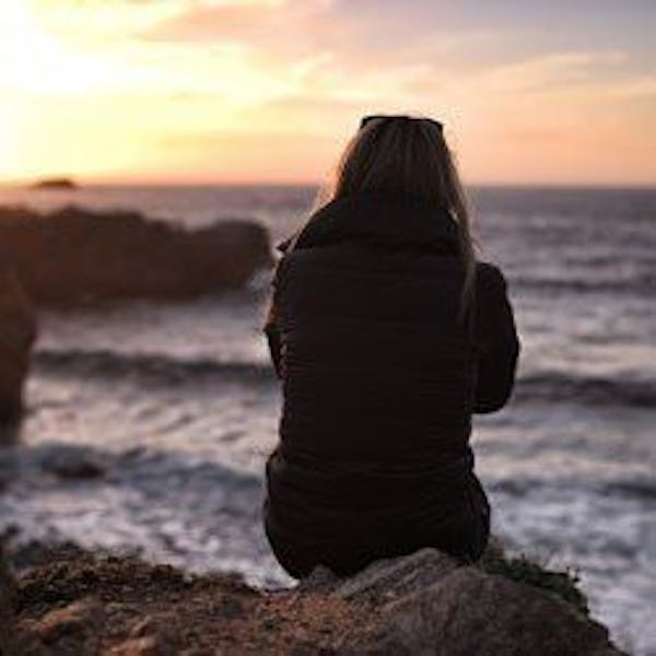 A woman enjoying a sunset by the coast alone