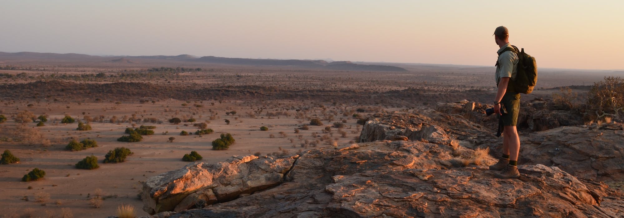 An ACE volunteer standing on a rocky outcrop in the African bush surveying the landscape at sunset
