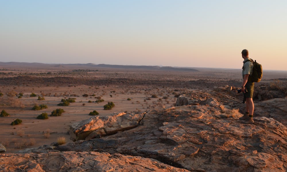 An ACE volunteer standing on a rocky outcrop in the African bush surveying the landscape at sunset