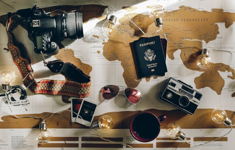 A map of the world on a desk with a passport, sunglasses, cameras and other objects scattered on top