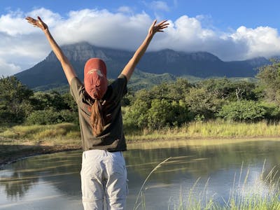 A girl cheers in front of a beautiful landscape at Moholoholo
