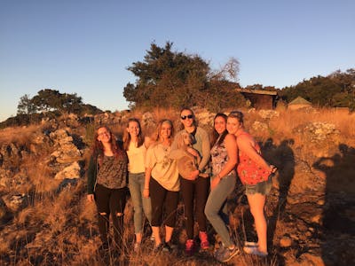 A group of happy ACE school students, posing in the sunset and cuddling a domestic dog