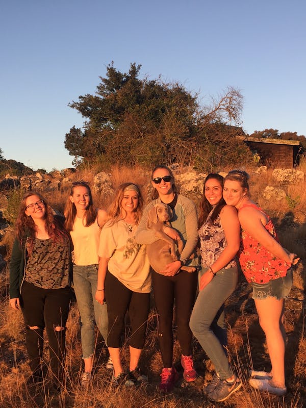 A group of happy ACE school students, posing in the sunset and cuddling a domestic dog