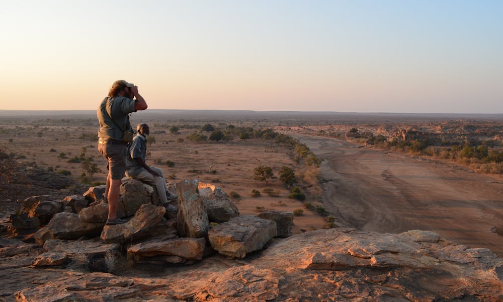 2 men surveying the landscape onto of a pile of rocks, high up in the African bush