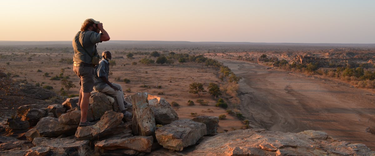 2 men surveying the landscape onto of a pile of rocks, high up in the African bush