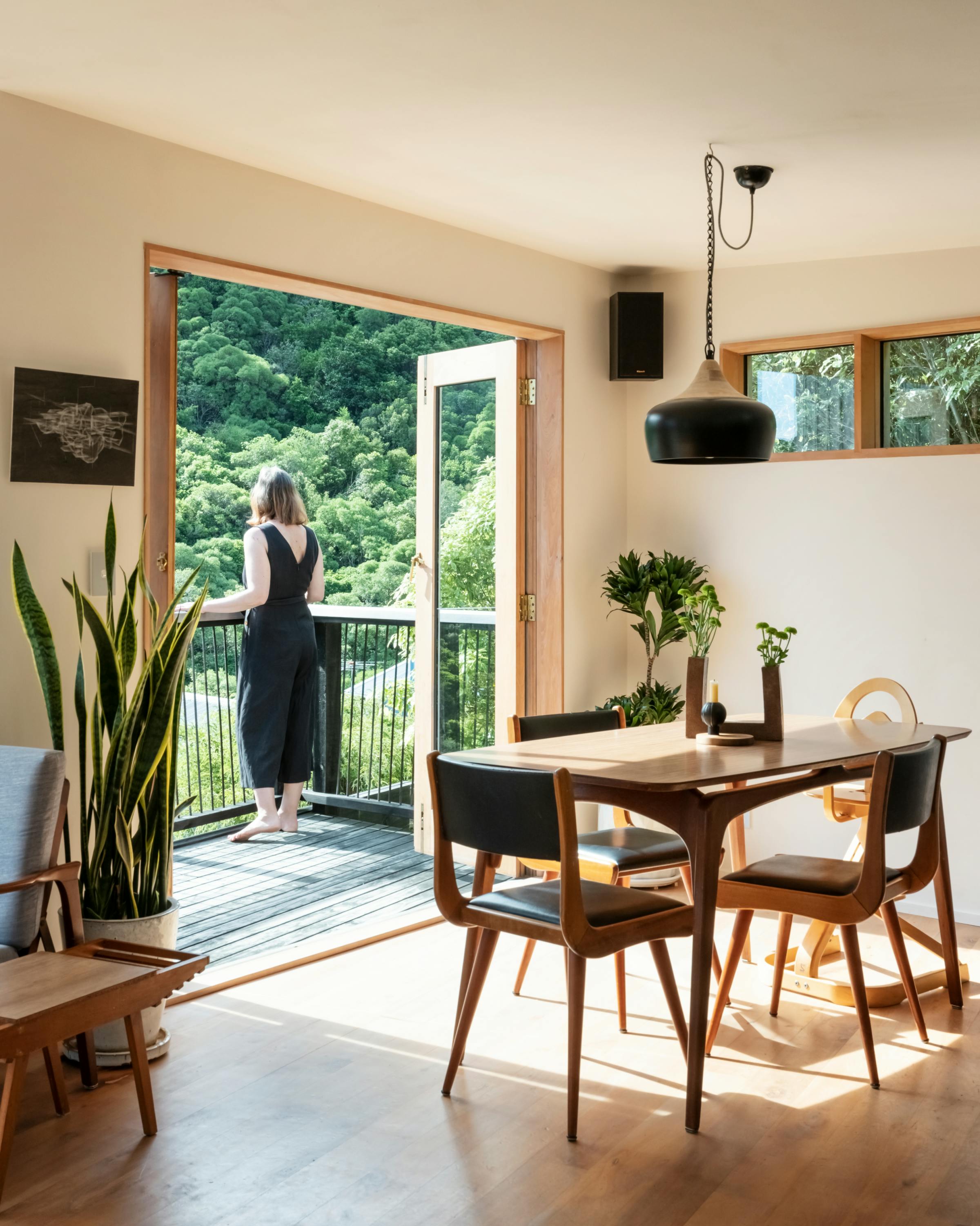 An interior view with the kitchen table and a deck overlooking native bush.