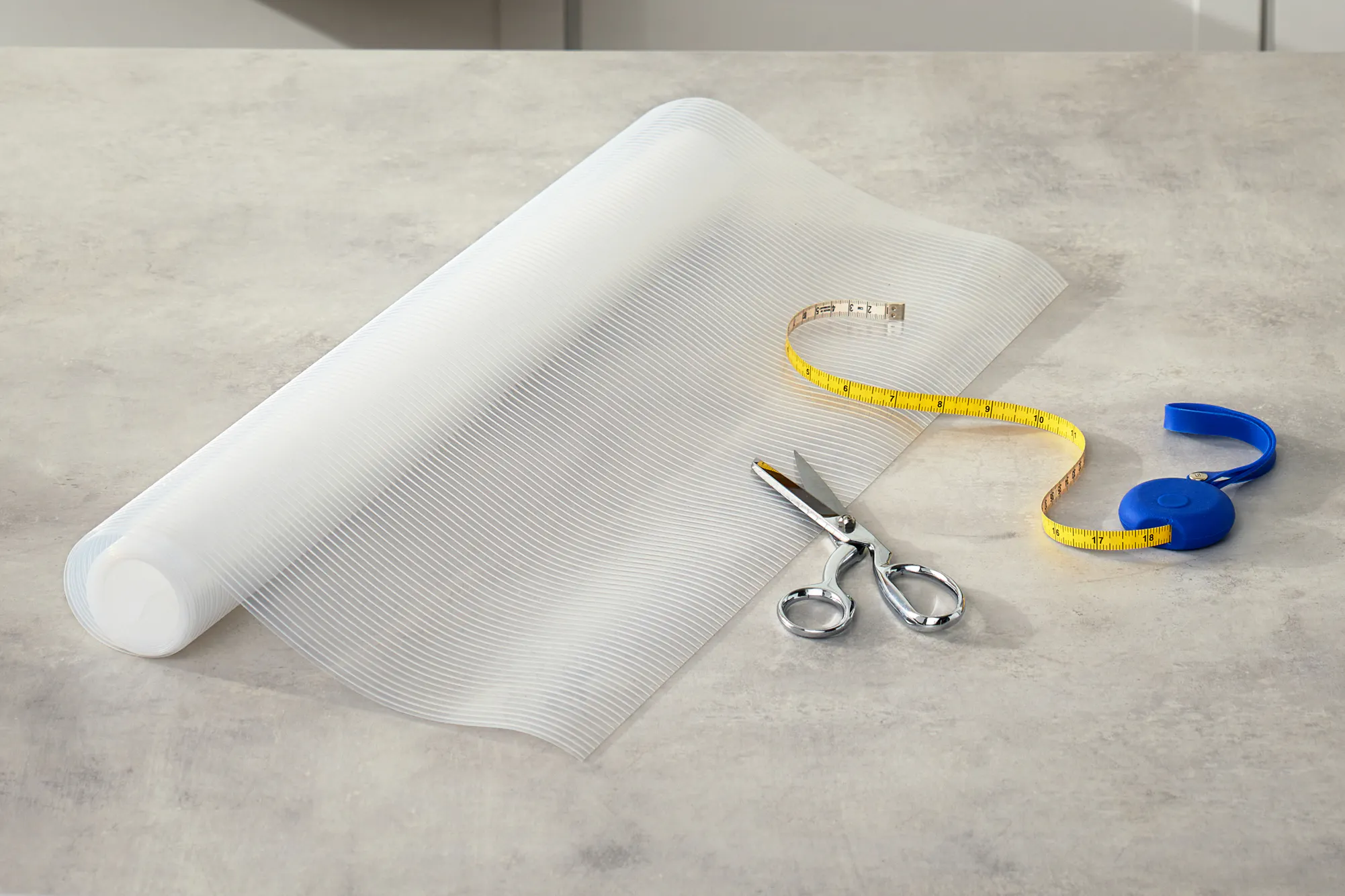 A roll of plastic shelf liner with a pair of scissors and measuring tape