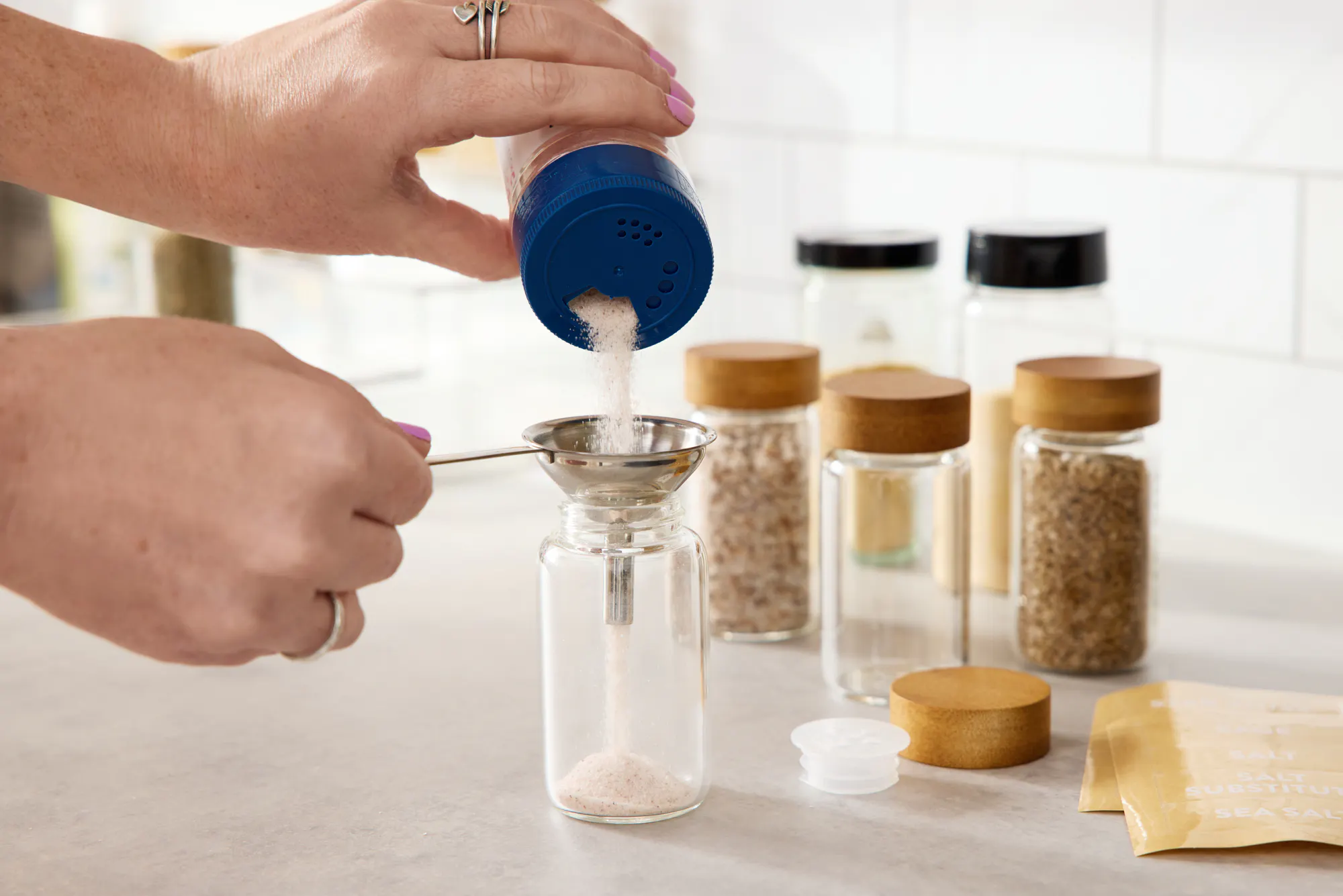 A person decanting spices into glass spice jars