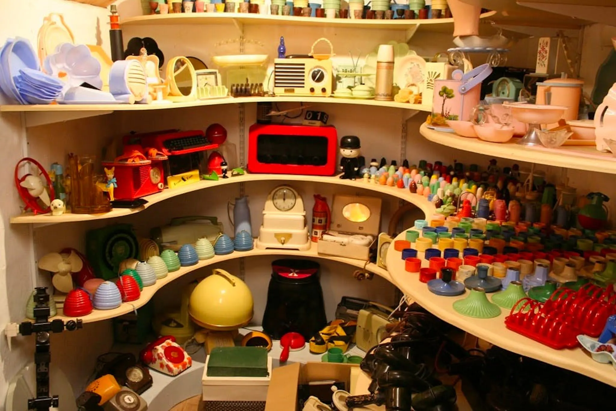 Photograph of shelves crowded with colourful mid-century plastic housewares, radios and kitchen goods