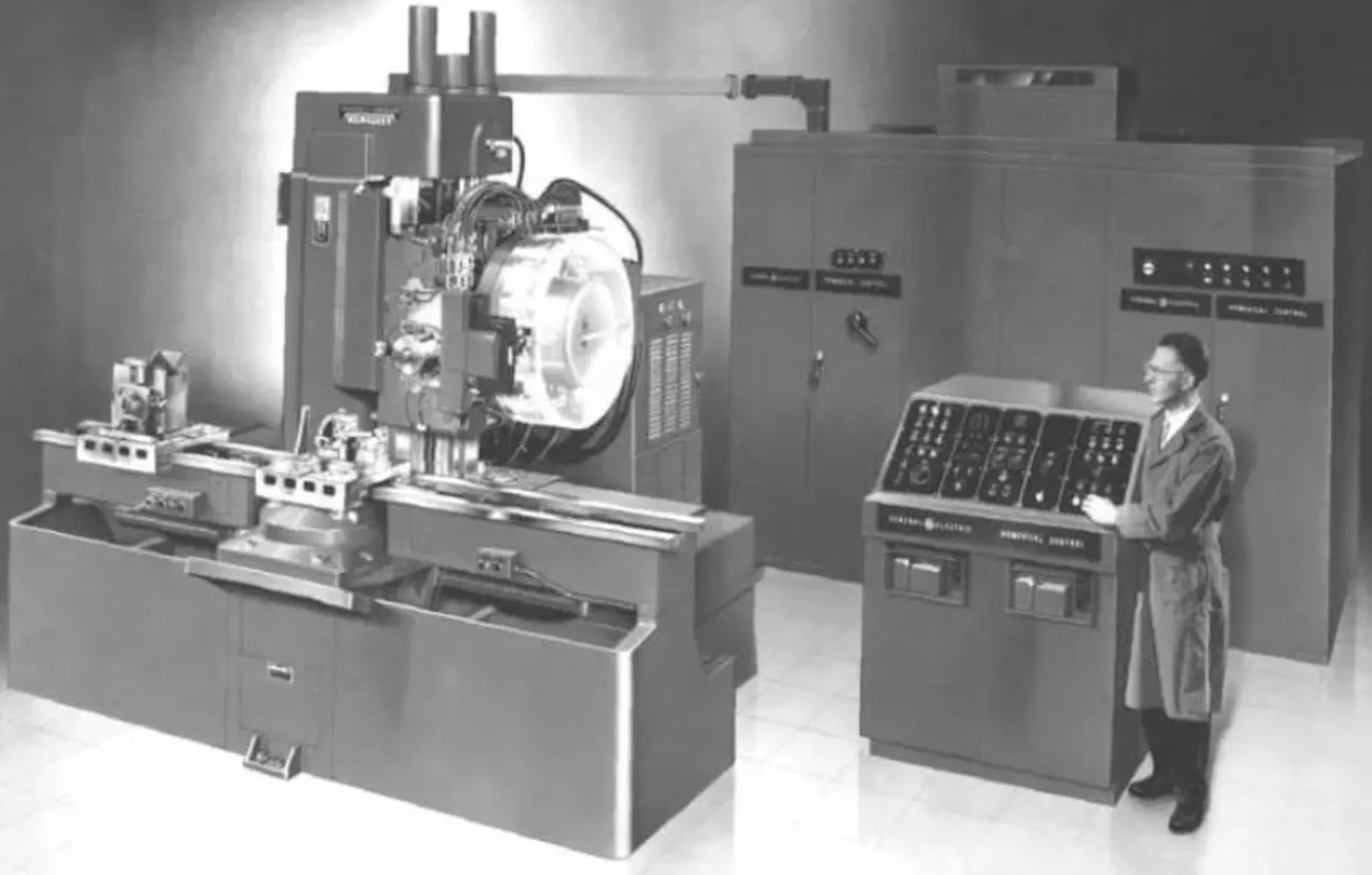 Black-and-white photograph of an operator at the console of an early numerically controlled milling machine