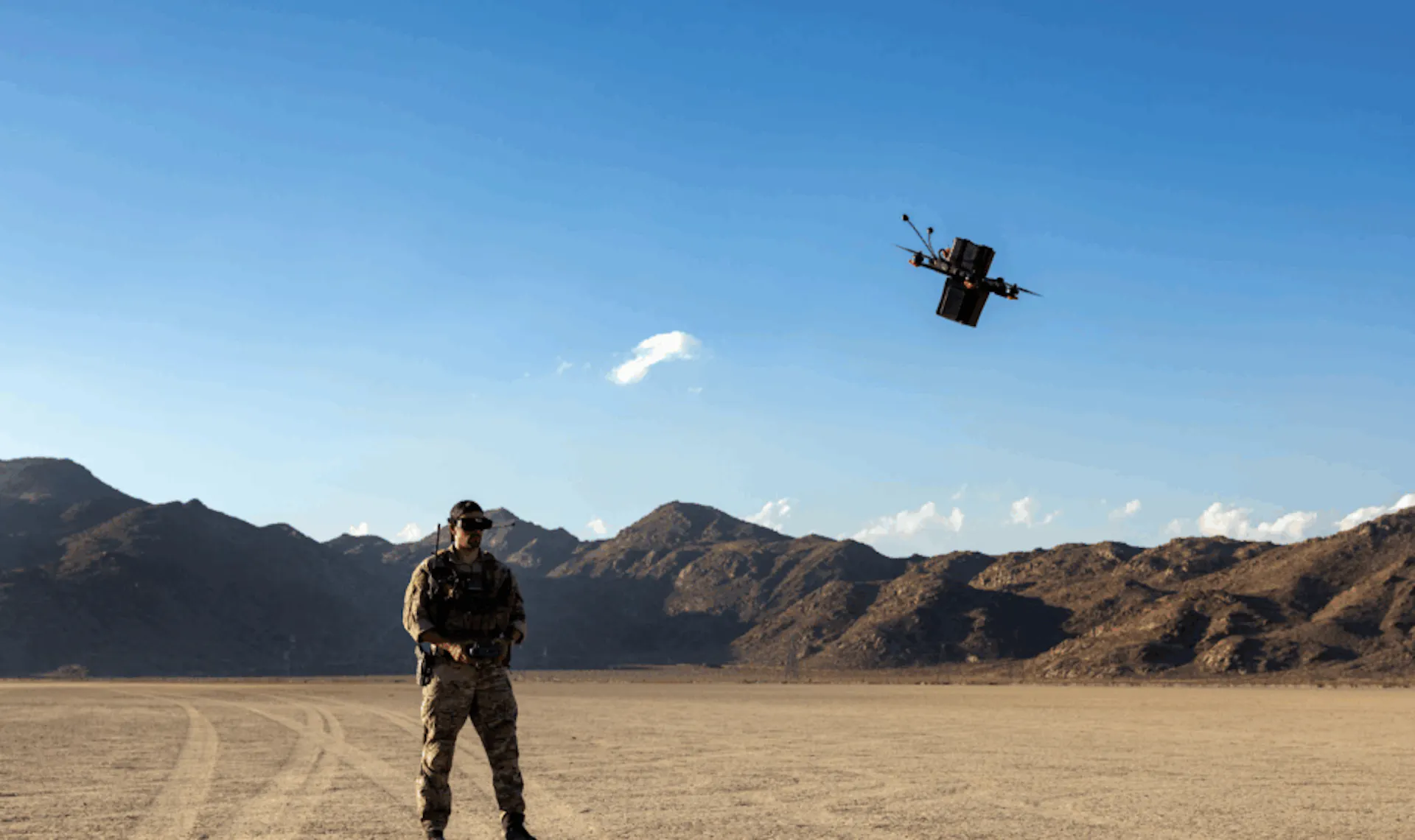A soldier stands on a desert lakebed beneath an FPV quadcopter carrying CX2's Vadris RF-seeking payload, a boxy sensor module mounted under the drone's frame.