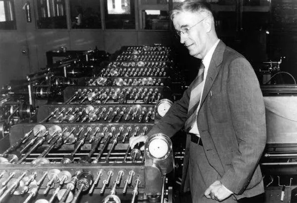 Black-and-white photograph of Vannevar Bush standing beside the differential analyser's banks of rotating shafts