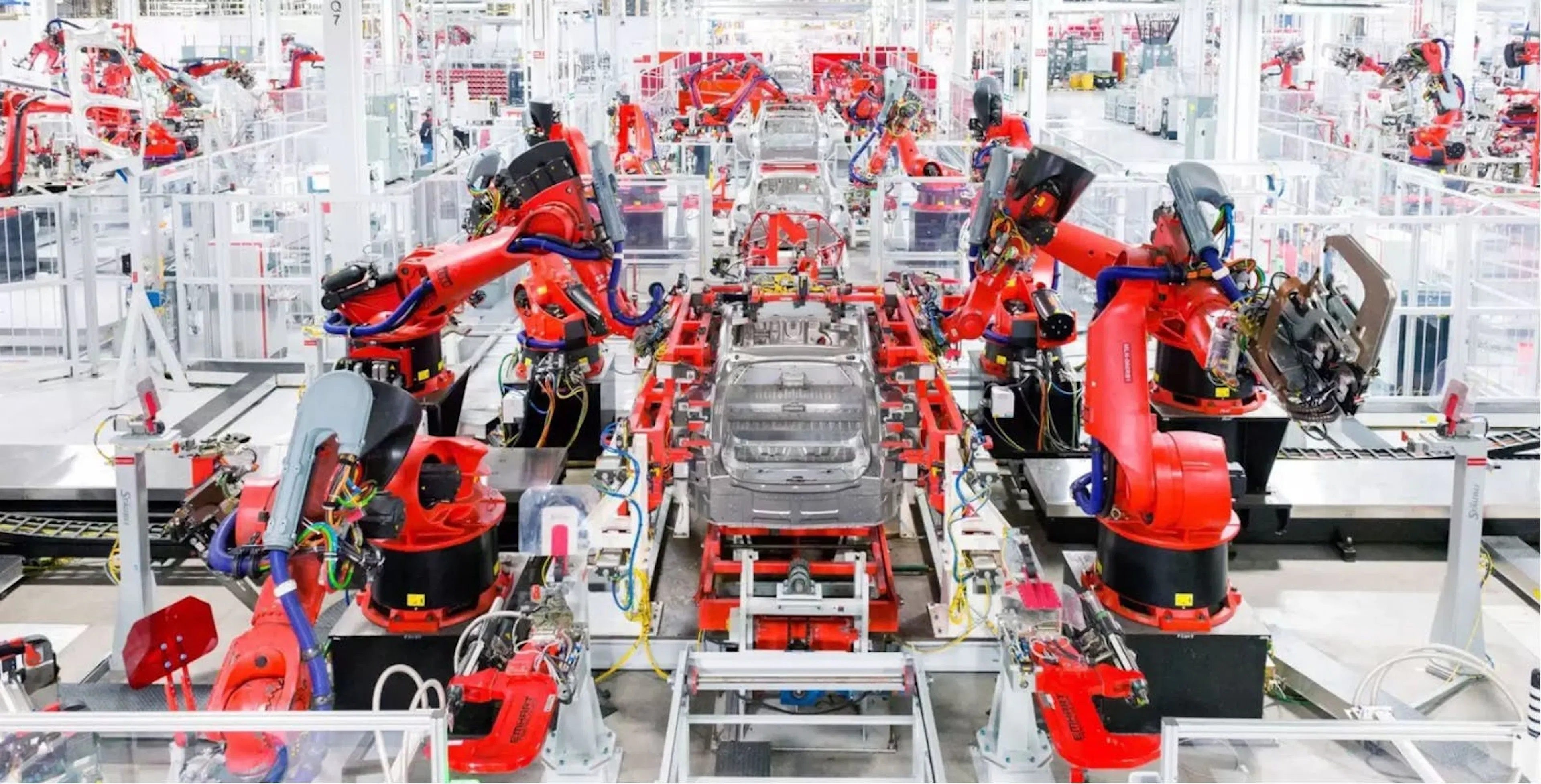 Photograph of an automotive assembly line where rows of red robotic arms work on car bodies