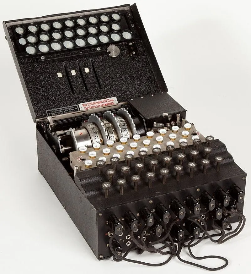 Photograph of a German Enigma machine with its lid open, showing rotors, keyboard and plugboard cables