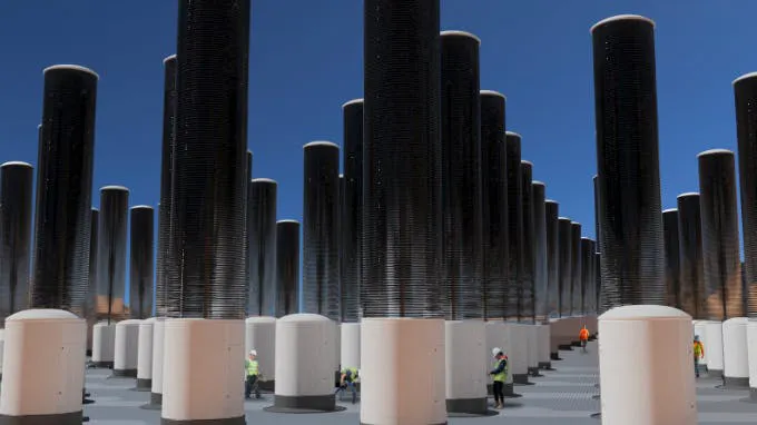 Photograph of tall cylindrical direct air capture towers in rows, workers walking between them